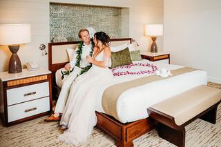 A couple enjoys a romantic moment in a cozy hotel room, adorned with flowers, celebrating their special day in an intimate setting.