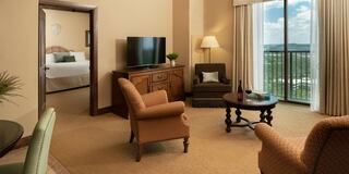 A spacious, elegantly furnished suite featuring a cozy seating area, a flat-screen TV, and a balcony with scenic views.