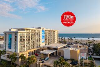 A contemporary beachfront hotel features modern architecture, a large mural of ocean waves, and a welcoming entrance amidst lush greenery.