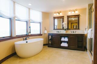 A bright, spacious bathroom features an elegant freestanding bathtub, wooden vanity with double sinks, and large windows for natural light.