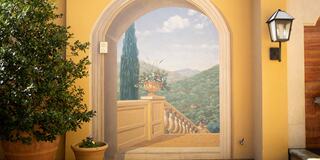 A sunny archway reveals a mural of a serene landscape, featuring distant hills and a decorative urn, surrounded by potted greenery.