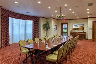A spacious conference room features a long table with water bottles and notepads, surrounded by beige chairs, with windows and decorative elements.