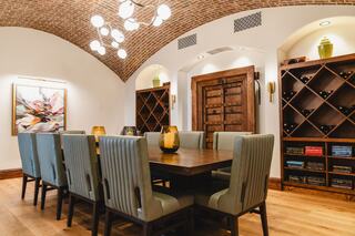 A stylish dining room features a large wooden table surrounded by cushioned chairs, accented by a brick ceiling and wine storage.