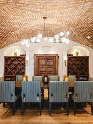 A stylish dining area features a wooden table, plush chairs, a striking brick arch ceiling, and elegant wine storage, creating an inviting atmosphere.