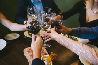 A group of friends raises their glasses in a toast, surrounded by a cozy dining setting with food on the table and warm lighting.