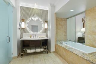 A modern bathroom features a double vanity with a circular mirror, elegant lighting, a soaking tub, and stylish tile accents throughout.