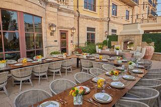 A beautifully set outdoor dining area features a long wooden table adorned with flowers, plates, and glasses, surrounded by stylish seating.