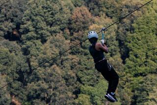 A person in a helmet glides on a zip line high above a lush green forest, enjoying an exhilarating outdoor adventure.