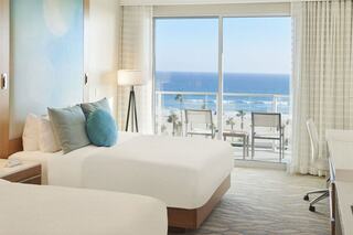 A bright, modern bedroom featuring two beds, large windows with ocean views, and a cozy atmosphere enhanced by soft furnishings.