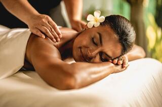 A woman enjoys a relaxing massage, adorned with a flower in her hair, exuding tranquility and bliss in a serene spa setting.
