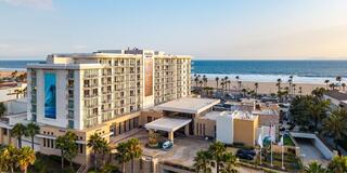 A modern beachfront hotel with palm trees and ocean views, featuring a spacious entrance and contemporary architecture under a clear sky.