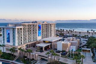A modern hotel near the beach features large windows, palm trees, and an ocean view, creating a coastal retreat ambiance.