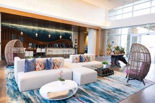 A stylish, modern lobby features a large sofa with colorful pillows, chic seating, a glass coffee table, and vibrant decor elements.