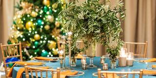 A beautifully set table with an elegant centerpiece, surrounded by candles, gold accents, and a decorated Christmas tree in the background.