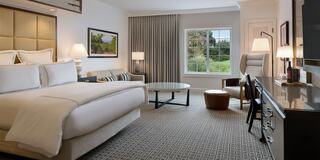 A modern luxury hotel room features a cozy bed, stylish furnishings, a seating area, and large windows with outdoor views.