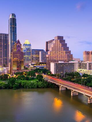 A vibrant urban skyline at dusk, featuring modern architecture, a tranquil river, and lush greenery, reflecting the city's dynamic spirit.