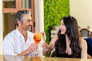 A joyful couple clinks glasses in a bright setting, enjoying drinks and sharing smiles, radiating happiness and connection.