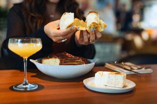 A person enjoys a delicious meal featuring pastries and a cocktail, savoring every moment in a cozy, inviting setting.