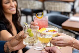 Cheers to good times! Four colorful cocktails are raised in a toast, with friends enjoying a lively and vibrant gathering.