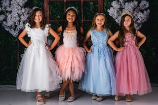 Four girls pose confidently in colorful, elegant dresses against a floral backdrop, showcasing joy and friendship.