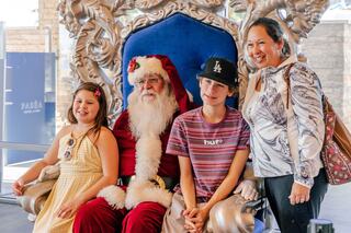 A festive Santa Claus poses with two children and an adult, all smiling, in a cheerful holiday setting.