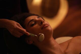 A serene woman relaxes during a soothing facial treatment, enjoying gentle movements with a jade roller against her skin.