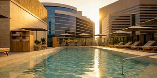 A serene rooftop pool area features lounge chairs, umbrellas, and modern architecture, illuminated by a warm sunset glow.