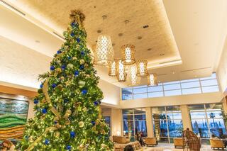 A lavishly decorated Christmas tree towers in a bright, modern lobby, complemented by elegant light fixtures and cozy seating areas.