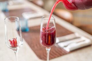 A vibrant red beverage is being poured into a tall glass, while a second glass with a decorative element sits nearby on a stylish table setting.