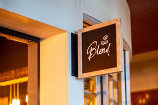 A wooden sign displays the word "Blend" in elegant script, hanging outside a chic café with warm lighting in the background.