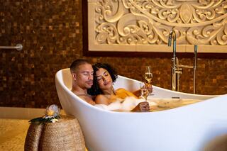 A couple relaxes in a luxurious bathtub filled with bubbles, sharing a romantic moment and champagne in an elegant setting.