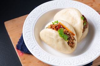 Steamed bao buns filled with savory shredded meat, topped with herbs and spices, served on a decorative plate.