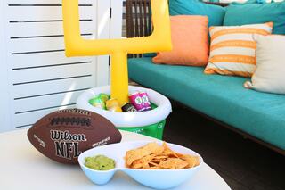 A football, snacks, and drinks are set up beside a colorful couch, with a yellow goalpost in the background, perfect for a game day gathering.