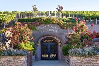 A charming spa entrance nestled among vibrant flowers and lush vineyards, featuring elegant stonework and inviting doors.