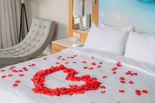 A cozy bed adorned with red rose petals arranged in a heart shape, set in a modern, inviting hotel room.