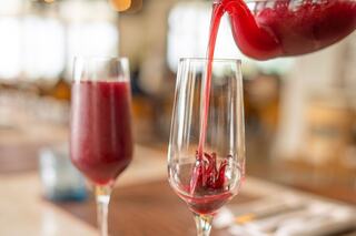 A vibrant red drink is elegantly poured into a flute, alongside another glass filled with the same beverage, set in a stylish dining environment.