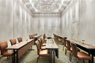 A stylish, well-lit meeting room featuring elegant wooden tables, plush chairs, and floral centerpieces, perfect for gatherings.