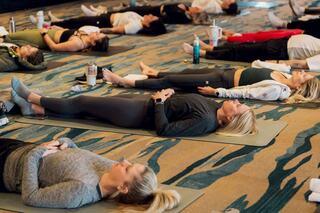Three women practice yoga in a serene studio, focusing on poses with dumbbells, against a warm, illuminated backdrop.