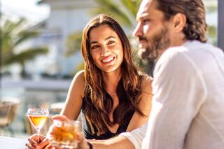 A woman enjoys a cocktail while seated at a stylish bar, surrounded by greenery and soft lighting, exuding a relaxed, confident vibe.