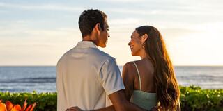 A couple shares a romantic moment by the ocean, enjoying a sunset, with warm smiles and gentle embraces reflecting their connection.