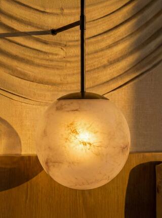 A glowing, spherical pendant light with a marble-like texture hangs from a sleek black fixture, casting warm light against a soft background.