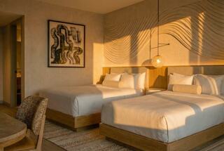 A stylish hotel room features two beds, modern decor, a unique art piece, and warm lighting, creating a cozy yet elegant atmosphere.