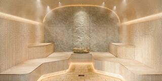 A serene spa environment with stone seating, soft lighting, and a central rock feature, creating a tranquil atmosphere.