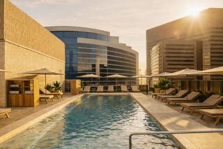 A sleek rooftop pool with lounging chairs and umbrellas, surrounded by modern buildings, bathed in warm sunlight during golden hour.