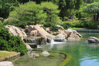A serene landscape features lush greenery, rocky formations, and a gentle waterfall cascading into a tranquil pond.