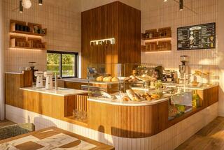 A cozy café with a wooden counter displays an array of baked goods, complemented by warm lighting and a minimalist design.