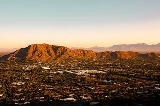 Golden sunlight bathes rugged mountains and a sprawling urban landscape, with distant peaks framing the serene horizon.