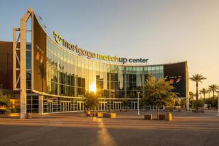 A modern building with large glass windows reflects sunset light, featuring the "Mortgage Matchup Center" sign and surrounded by palm trees.
