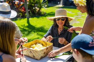 A group gathers outdoors, crafting together with a basket of flowers, sharing smiles and laughter on a sunny day.