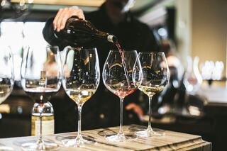 A person pours red wine into elegantly shaped glasses, surrounded by an array of wines in a stylish setting.